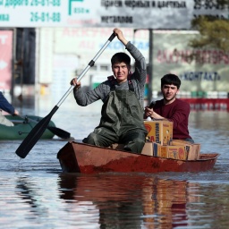 Zwei Männer rudern ein Boot durch das Hochwasser eines überschwemmten Gebiets, um Lebensmittel auszuliefern.