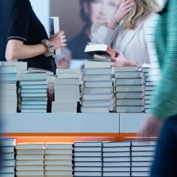 An einem Tisch auf dem sich Bücher stapeln, stehen Menschen, die Bücher in den Händen halten