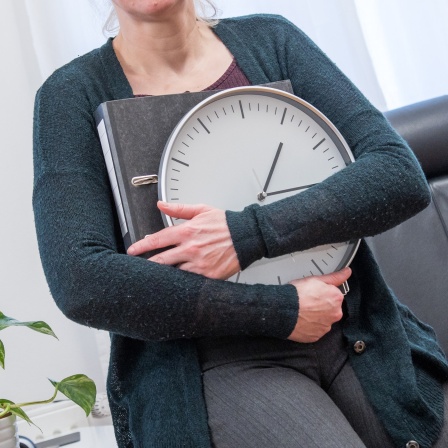 Eine Frau sitzt in einem Büro und hält eine Uhr in der Hand 