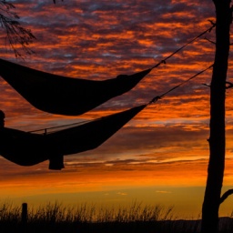 Jemand liegt in einer Hängematte, im Hintergrund ist der Abend-/Morgenhimmel rot gefärbt