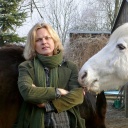 Die Schriftstellerin Karen Duve steht im Freien links neben einem Schimmel, dessen Kopf von rechts ins Bild ragt. Sie trägt eine hellgrüne Jacke und einen Wollschal in der gleichen Farbe.