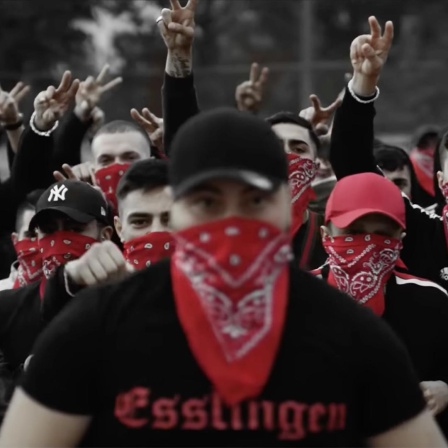 Screenshot aus dem Musikvideo "Eska - Bumaye". Eine Gruppe vermummter junger Männer mit der Aufschrift "Esslingen" auf schwarzer Kleidung. Rapper Eska wird mit einer Bande in Verbindung gebracht. In seinen Musikvideos inszenieren sich Männer als Gangster.