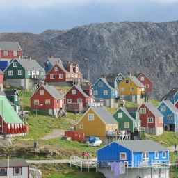 Der Ort Upernavik in Grönland. Bunte Häuser stehen in einer wunderschönen Naturlandschaft. Um die Häuser wächst grünes Grass. Im Hintergrund ein Fels.