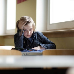 Ein Kind sitzt alleine in einem Klassenraum.