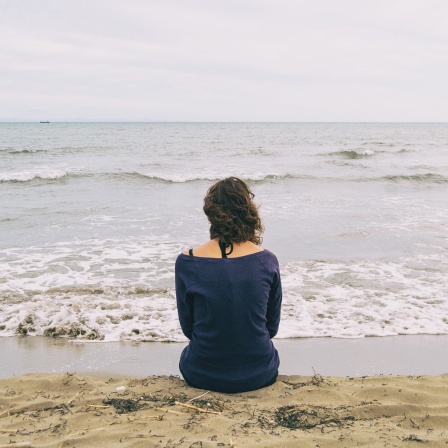 Eine Frau sitzt am Meer.