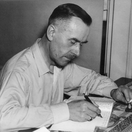 Thomas Mann sitzt schreibend und rauchend am Tisch. (um 1930)