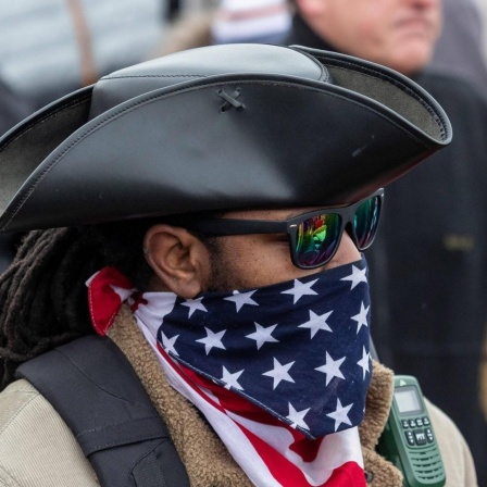 Pro-Trump-Demonstrant mit Sonnenbrille, Cowboyhut und vor den Mund gebundenem Tuch mit dem Motiv der US-Nationalflagge.