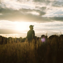 Ein Filmstill aus "All of Us Strangers": Ein Mann steht auf einem weiten Feld, die Sonne bricht durch die Wolken.