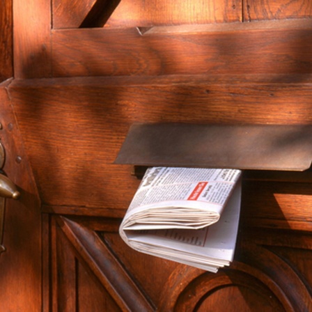 Eine Tageszeitung steckt in dem Briefkasten einer alten Holztür.  