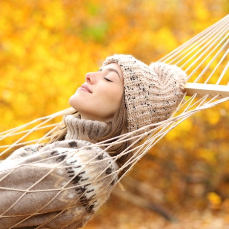 Eine Frau schläft in einer Hängematte in einem Herbstwald.