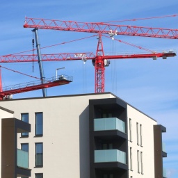 Das Beitragsbild des Dok5  Feature "Wohnungsmangel: Engpass oder Dauerkrise?" zeigt Wohnungsbau in der Stadt. Rote Baukräne stehen vor Neubauwohnungen.