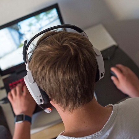 Ein junger Mann sitzt mit einem Headset vor einem Laptop