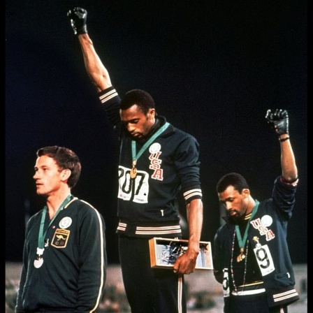 Tommie Smith (m) und John Carlos (re) heben bei der Ehrung zu Gold und Bronze die Faust mit schwarzen Handschuhen in die Höhe