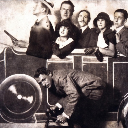 Max Morise, Simone Breton, Paul Eluard, Joseph Delteil, Gala Desnos, André Breton und Max Ernst (auf dem Fahrrad), auf dem Markt von Montmartre, 1923.