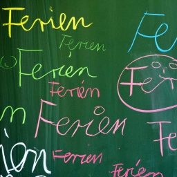 Auf einer Schultafel steht in verschiedenen Farben das Wort "Ferien"