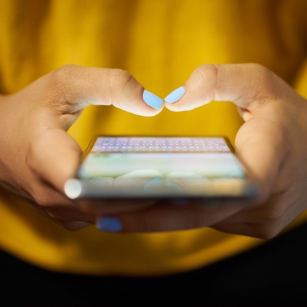 Die SMS wird am 3. Dezember 2017 25 Jahre alt. Mit dem Smartphone tippt eine Frau in einer gelben Bluse eine Textnachricht.