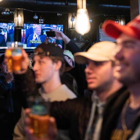 Junge Männer mit Getränken in den Händen schauen während einer Party die Inauguration von Donald Trump.
