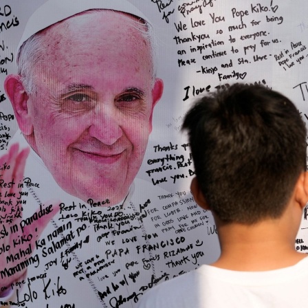 Auf eine Tafel mit einem Foto von Papst Franziskus schreibt ein junger Mann Dankesworte.