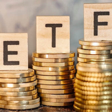Mehrere Stapel mit Münzen und dem Begriff ETF und einem Chart mit Börsenkursen. (Symbolfoto)
