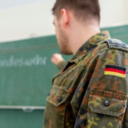 Ein Bundeswehrsoldat von der Seite vor einer Tafel, auf der Bundeswehr zu lesen ist.