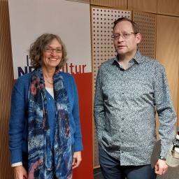 Eine Frau und ein Mann stehen nebeneinander in einem Studio. Im Hintergrund hängt ein Banner mit der Aufschrift NDR Kultur.