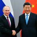 Der russische Präsident Putin und der chinesische Präsident Xi Jinping reichen sich die Hand. Hinter ihnen die Landesfahnen.