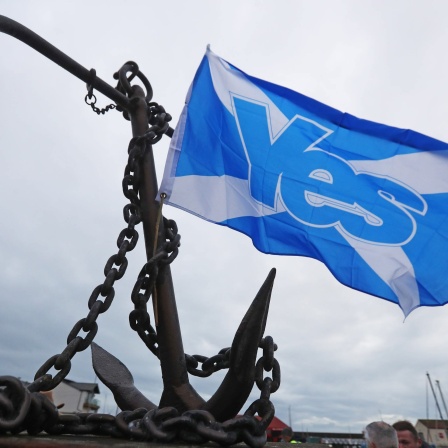 Eine blaue schottische Fahne mit Werbung für die Unabhängigkeit weht neben einem rostigen Anker, offenbar in einem Hafen