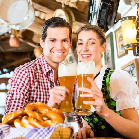 Mann und Frau in Tracht mit je einem Bierglas in der Hand: Deutsche Männer trinken mehr als sechsmal so viel Bier wie die Frauen. Die Gründe sind unklar. Zum einen trinken Männer grundsätzlich mehr Alkohol. Aber beim Bier sind die Unterschiede besonders auffallend.