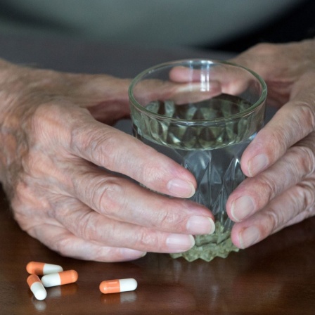 Ein älterer Mensch mit einem Wasserglas in der Hand und bereit gelegten Tabletten