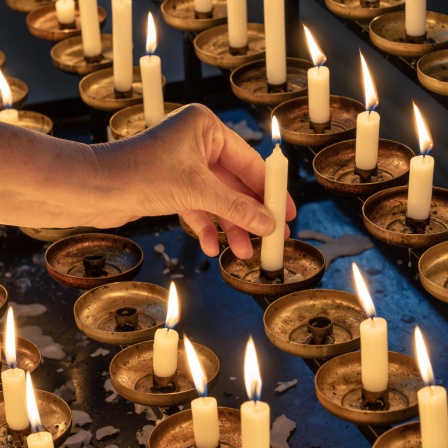 Frau zündet Opferkerze in einer Kirche an, um für ein persönliches Anliegen zu beten