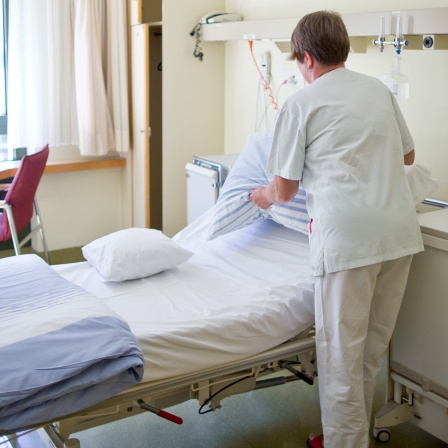 Eine Krankenpflegerin bereitet in einem Krankenzimmer ein Patientenbett vor.