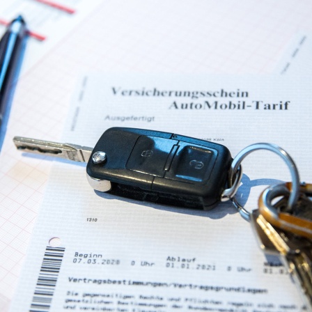 Auf dem Bürotisch liegt ein Autoschlüssel, Kugelschreiber und eine KFZ Versicherungspolice mit dem aktuellen KFZ Tarif Beitragssatz zur Fahrzeug Versicherung.