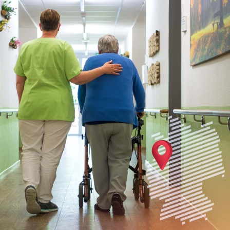 Pflegefachkraft geht mit einer Seniorin den Flur entlang. 