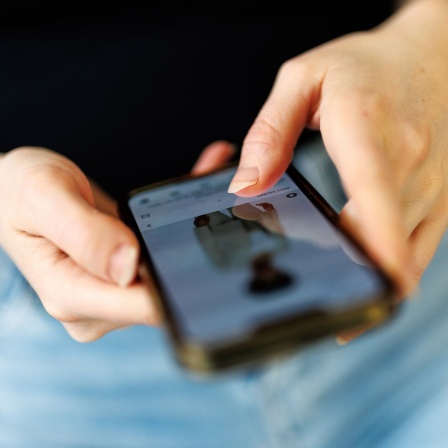 Symbolfoto: Eine junge Frau siet ein Foto in den sozialen Medien an.