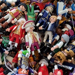 Viele bunte Spielfiguren von Playmobil mit unterschiedlicher Kleidung und verschiedenen Gegenständen liegen in einem Haufen aufeinander.