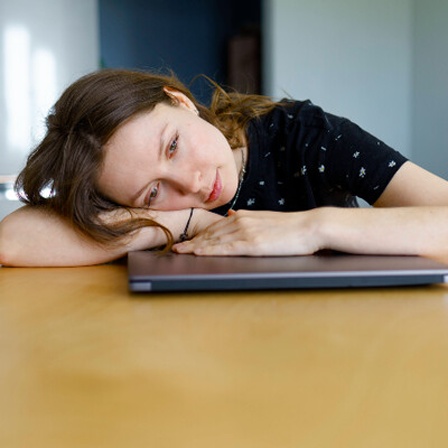 Eine Frau liegt auf ihrem zugeklapptem Laptop.