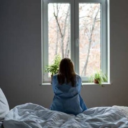 Frau sitz auf Bett und schaut aus dem Fenster.