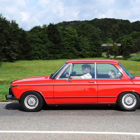 Ein roter BMW fährt über eine Landstrasse und ist von der Seite zu sehen