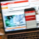 Auf einem Smartphone ist eine Eilmeldung eines Nachrichtenmagazins zur Corona-Krise angezeigt, das an einem Bildschirm mit Online-Angeboten von einigen überregionalen Zeitungen und Nachrichtenmagazinen steht.