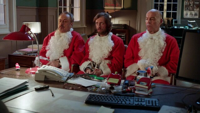 Drei Weihnachtsmänner vor einem Schreibtisch sitzend.