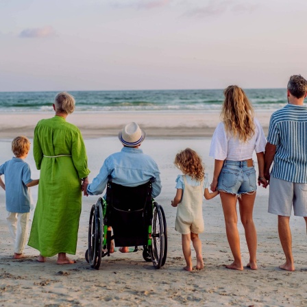 Kinder, Eltern und Großeltern stehen am Strand und blicken aufs Meer. 