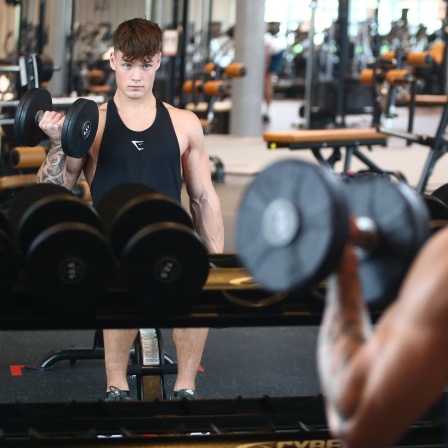 Junger Mann mit Hantel vor einem Spiegel im Fitnessstudio, Symbolbild