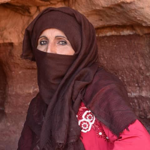 Die 48-jährige Wanderführerin Umm Yasser ist in der Höhle hinter ihr aufgewachsen. Durch die Corona-Pandemie kommen derzeit keine Touristen in ihr Tal auf der Sinai-Halbinsel. Sie trägt ein rotes Kleid und ein bräunliches Tuch um den Kopf.