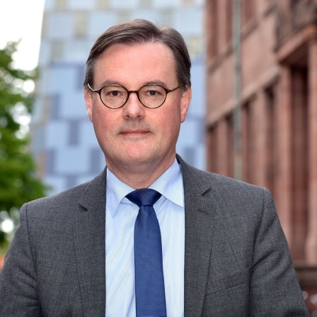 Ein Mann mit kurzen dunklen Haaren und Brille blickt in die Kamera