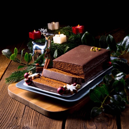Aufgeschnittener Lebkuchen liegt auf einem Tablet, umgeben von einem Adventskranz