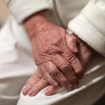 Nahaufnahme von zwei Händen eines alten Menschen, die übereinander liegen - die eine Hand scheint die andere festzuhalten.
