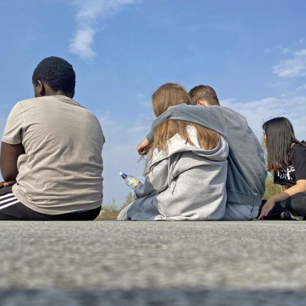 Vier Jugendliche sitzen auf einer Mauer im Riemer Park in München.