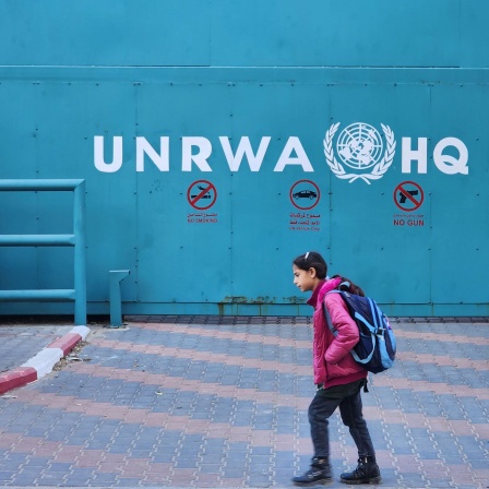 Ein Mädchen geht an der Aufschrift "UNRWA HQ Gaza" in Gaza City vorbei (Bild: picture alliance/ZUMAPRESS/Ashraf Amra)
