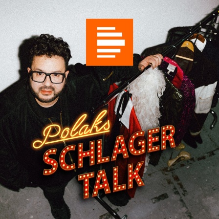 Polaks Schlagertalk: Podcast-Host Oliver Polak steht neben einer Garderobenstange mit bunten Bühnenoutfits wie Federboa und Glitzeranzügen