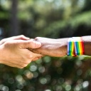 Zwei Menschen mit Regenbogenarmbändern halten sich an den Händen